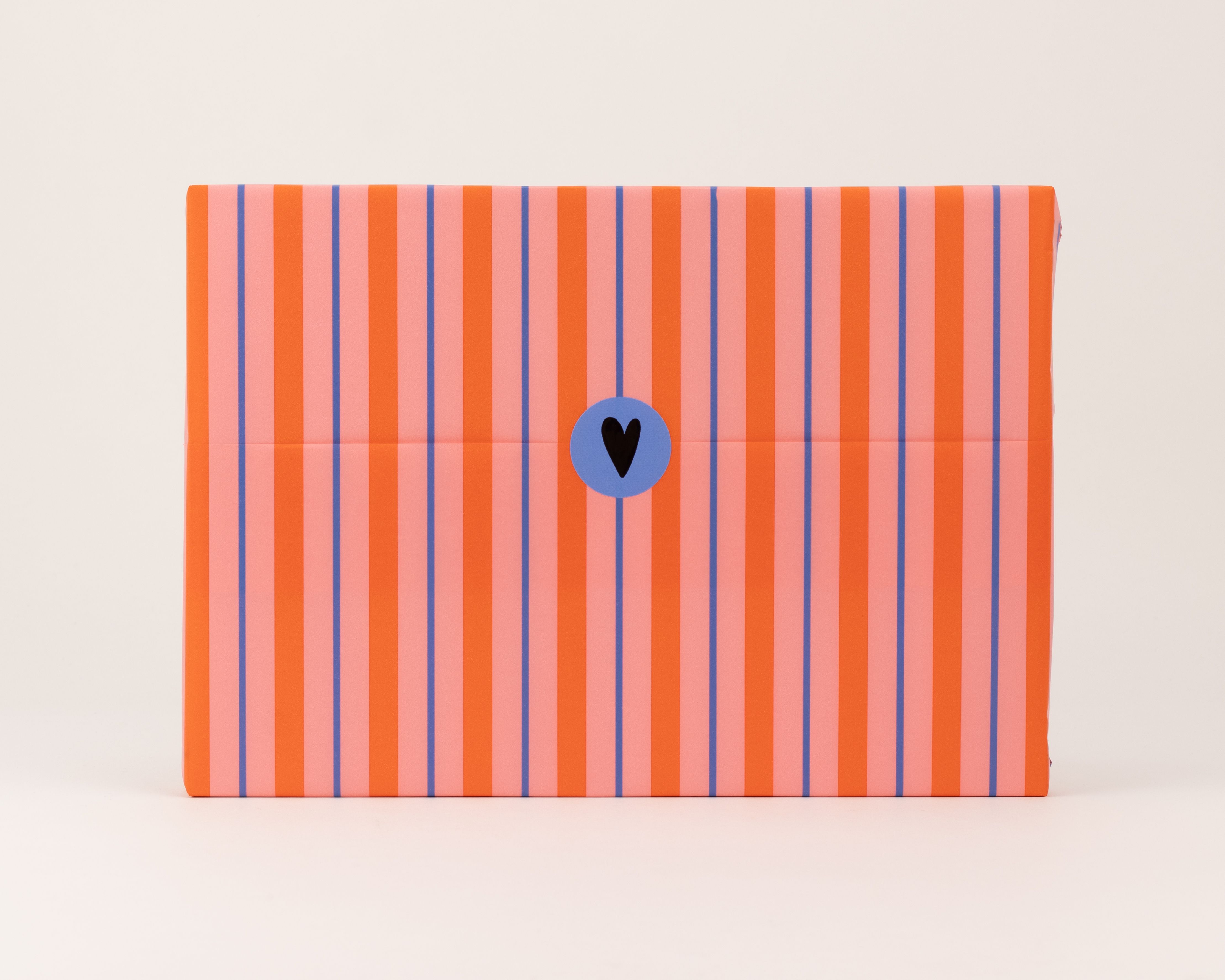 Seidenpapier mit Streifen in Pink, Rot und Blau. Darauf ein runder blauer Aufkleber mit schwarzem Herzmotiv