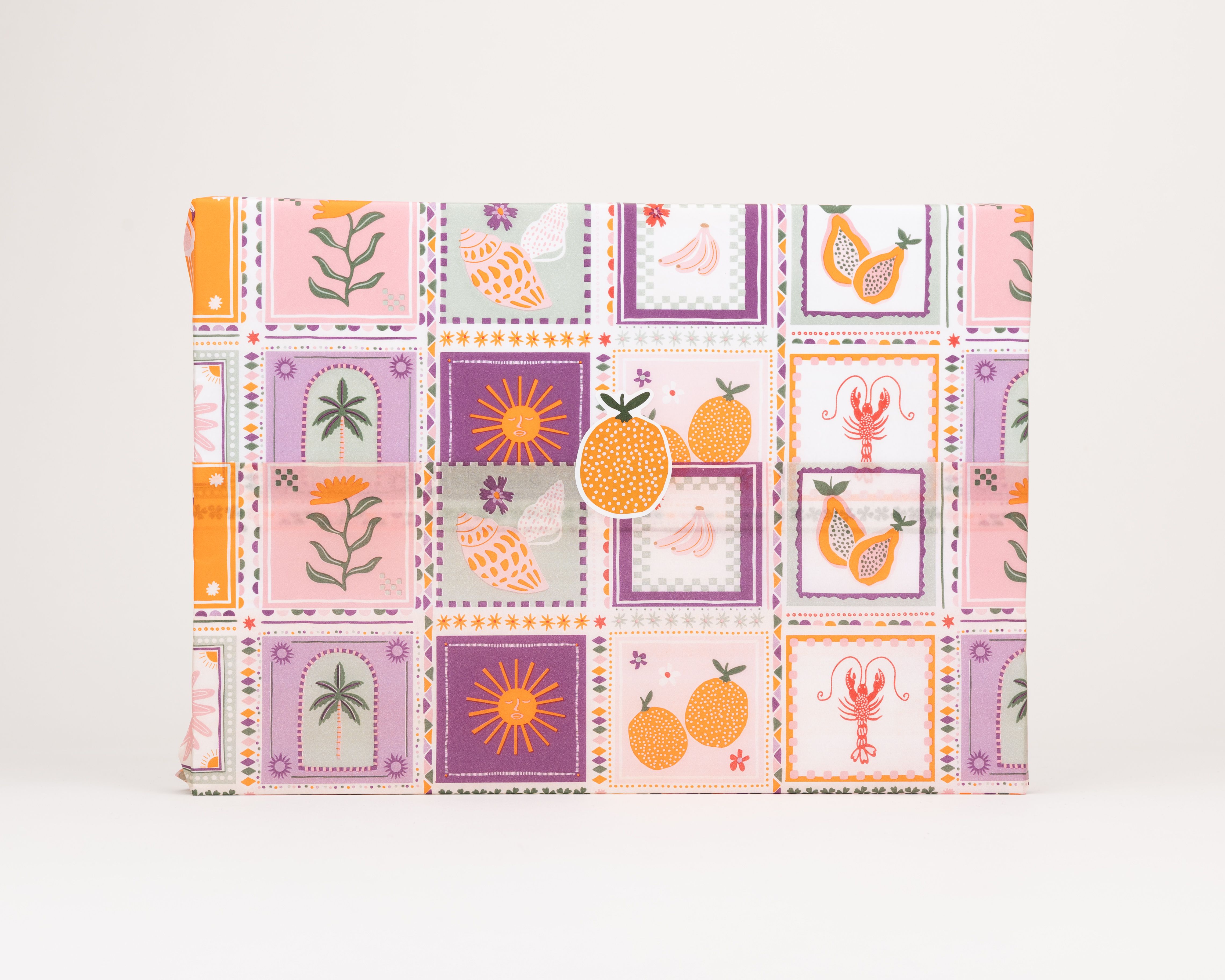 Seidenpapier mit buntem Sommermotiv-Design, das Palmen, Muscheln, Früchte und Sonnen zeigt. Darauf ein Aufkleber mit zwei Orangen.