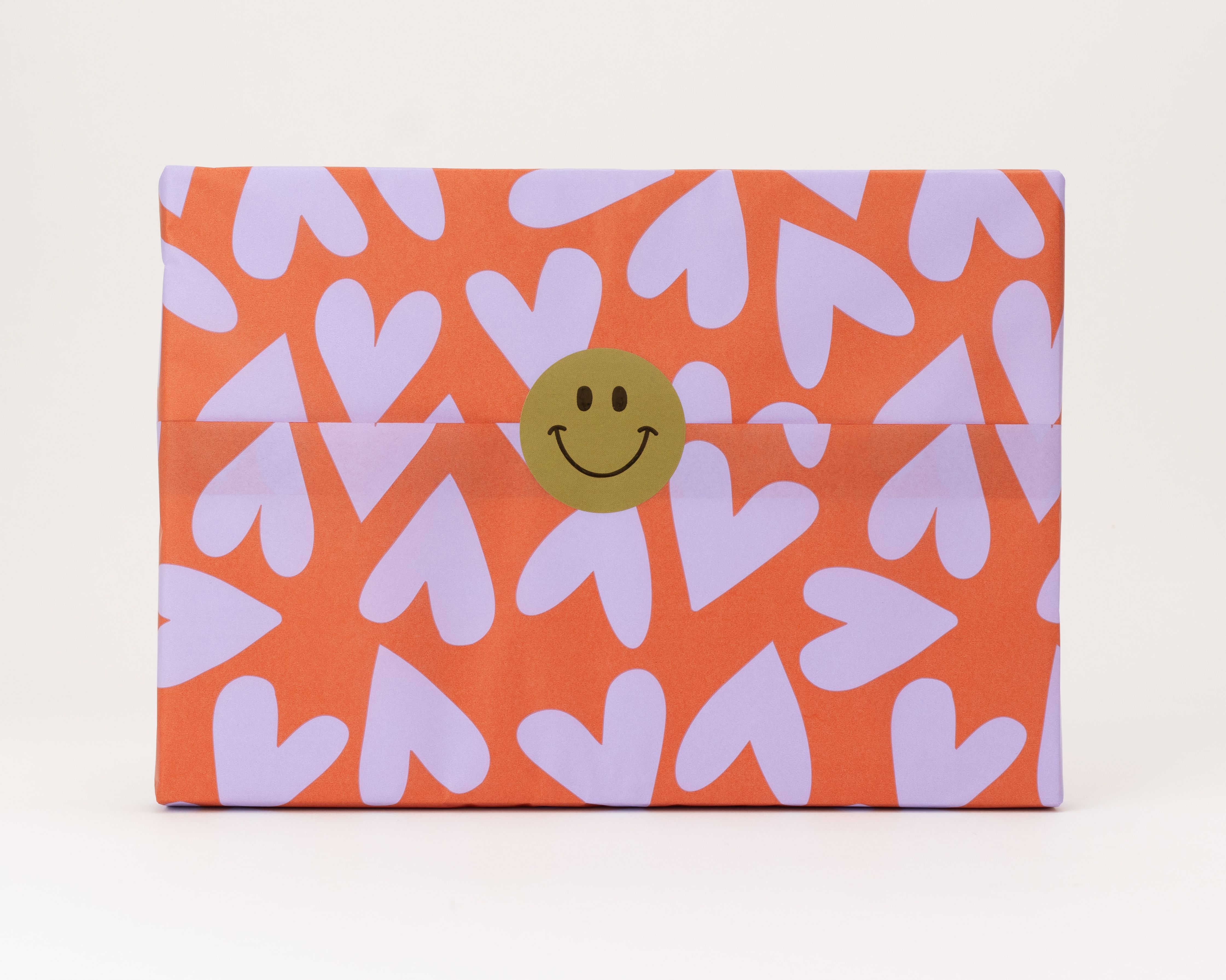 Seidenpapier auf Rolle, orange mit vielen lavendelfarbenen Herzen als Muster und einem grünen Smiley-Aufkleber vorne