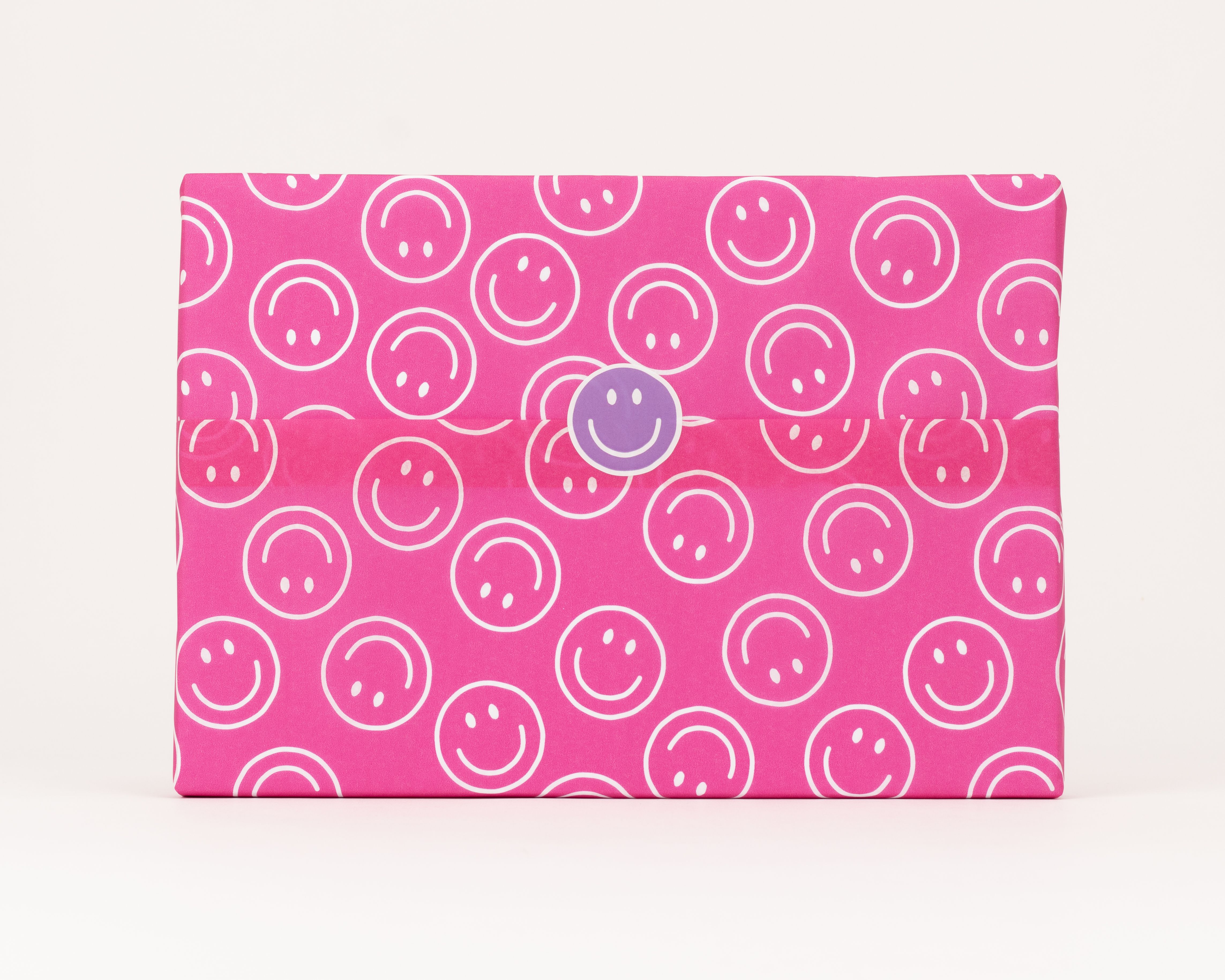 Seidenpapier in Pink mit weißem Smileys Muster. Darauf ein runder lila Aufkleber mit einem weißen Smiley