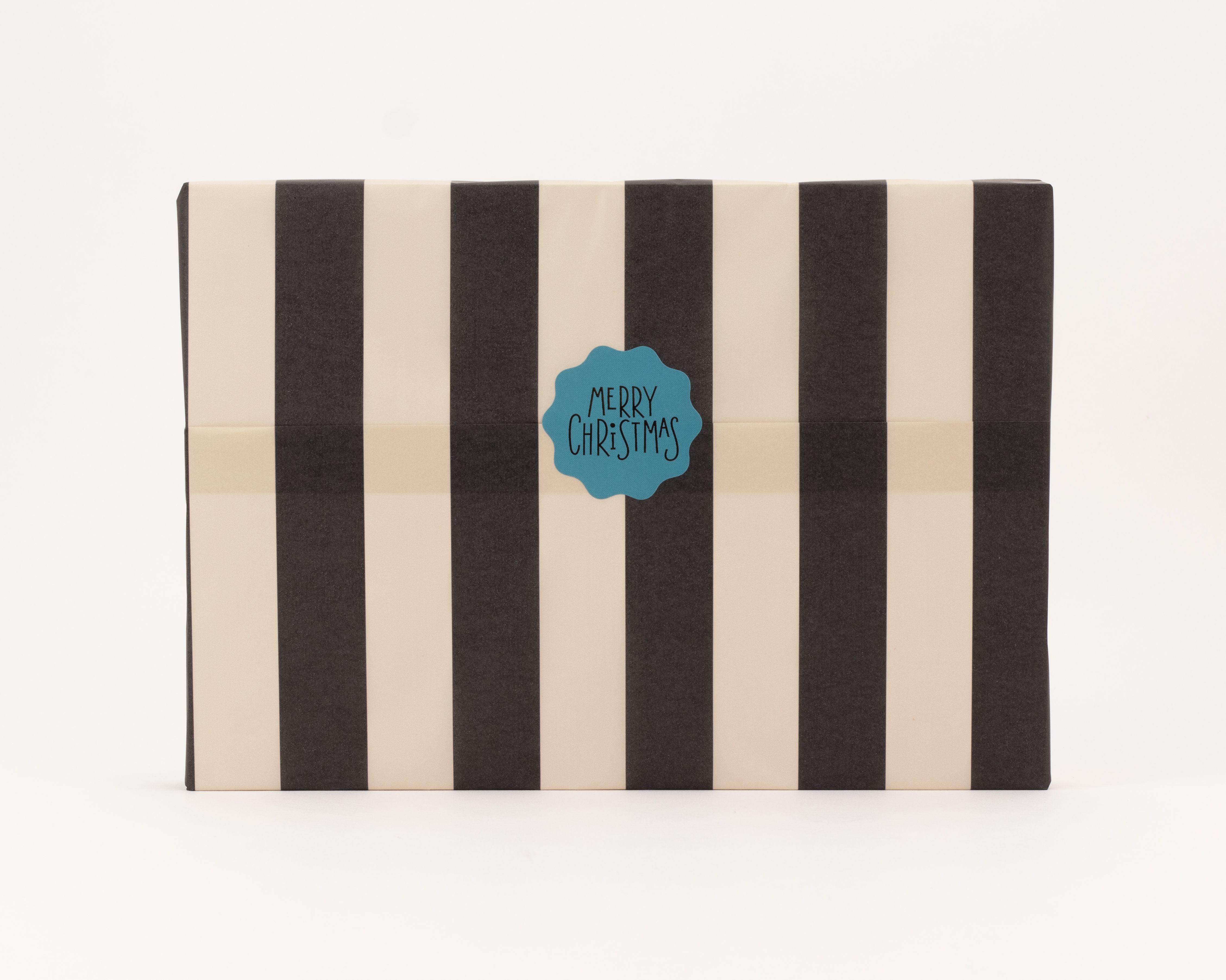 Seidenpapier mit vertikalen Blockstreifen in Schwarz und Beige. Ein gewellter türkisfarbener Aufkleber mit 'MERRY CHRISTMAS' Text