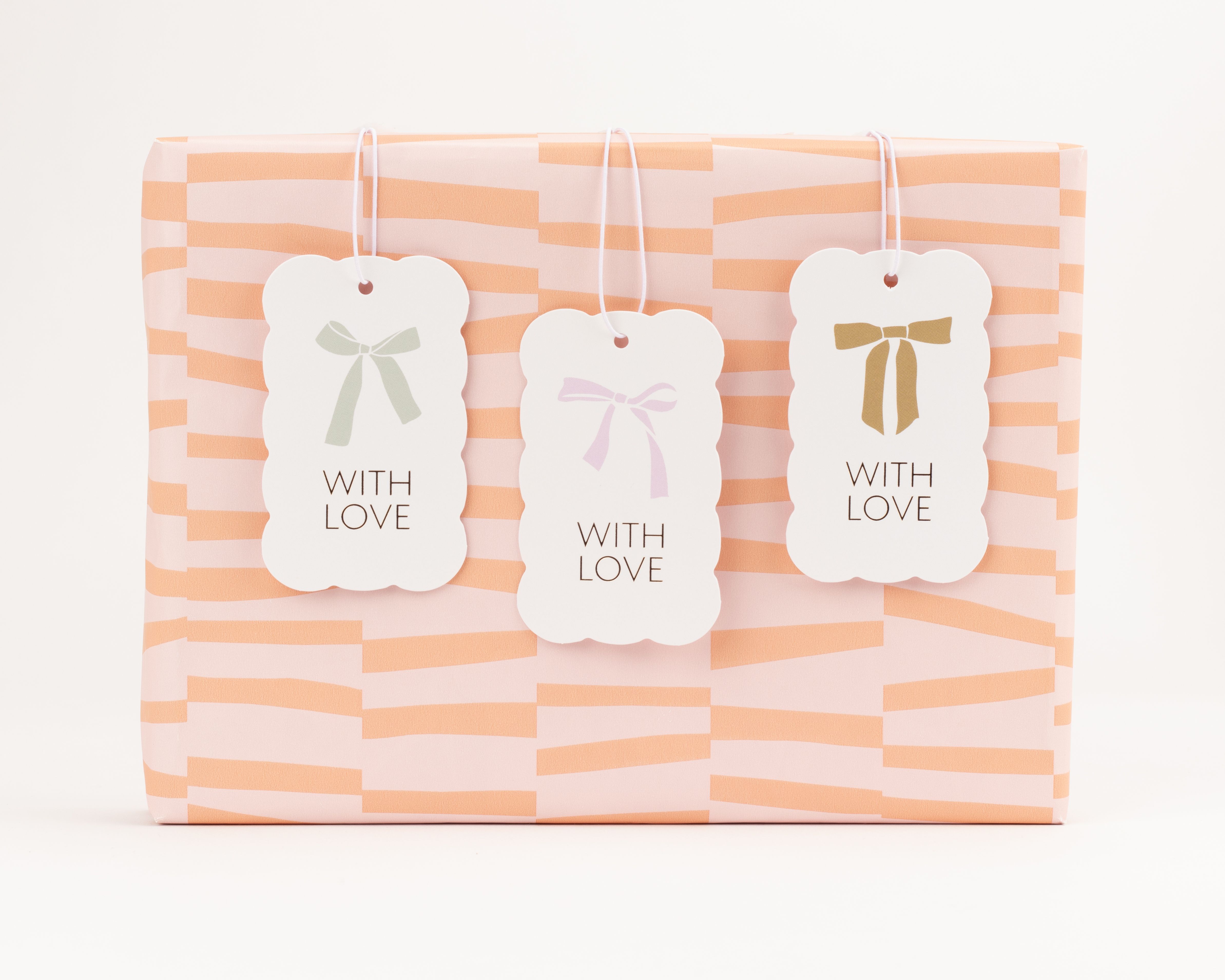 Geschenkanhänger-Set mit drei weißen Anhängern in gewellter Form, bedruckt mit Schleifenmotiven in Hellgrün, Hellrosa und Goldfarben