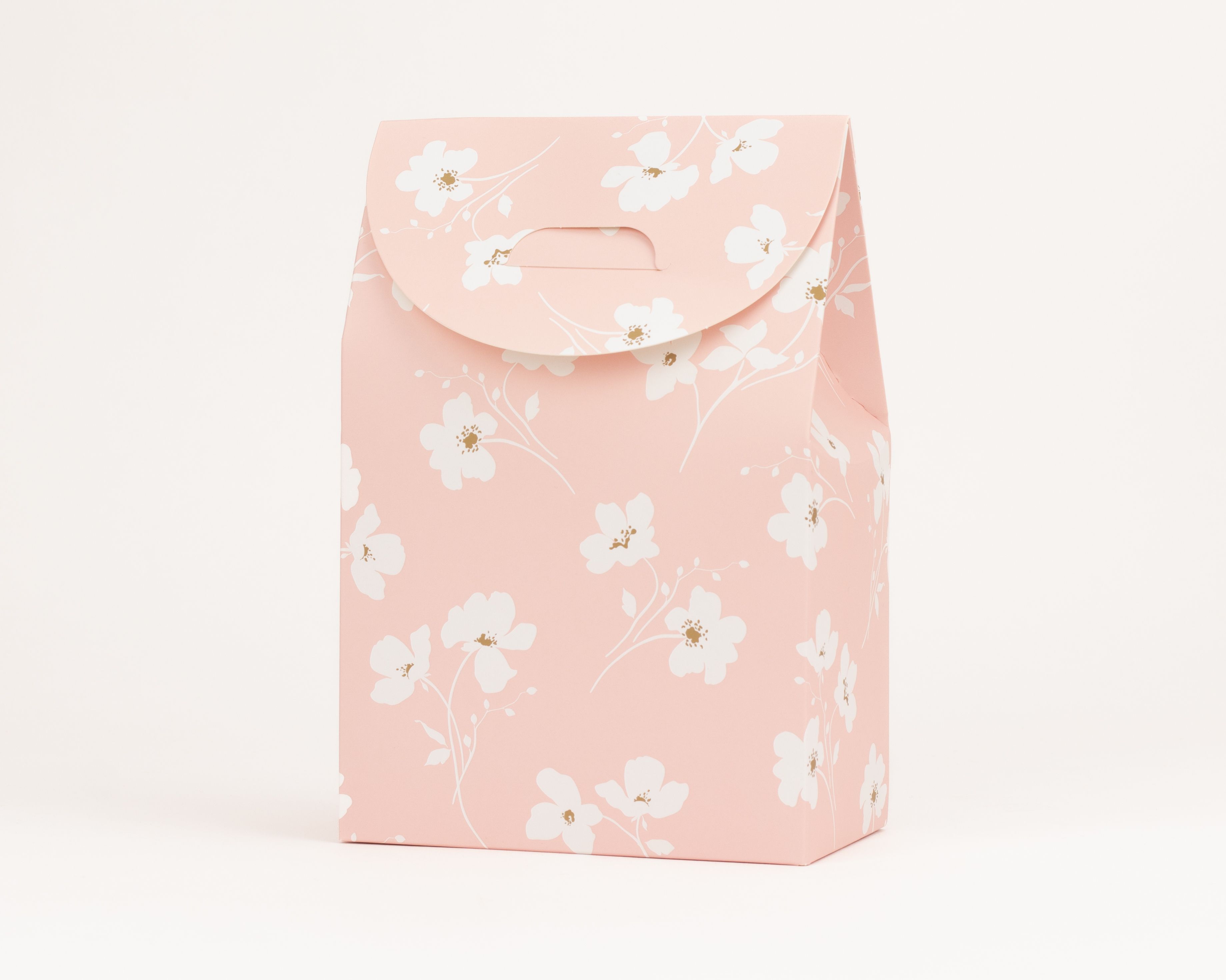 Geschenkboxen sind rechteckige Schachteln in Hellrosa mit einem weißen Wiesenblütenmuster und goldenen Blütenmitten sowie integriertem Tragegriff